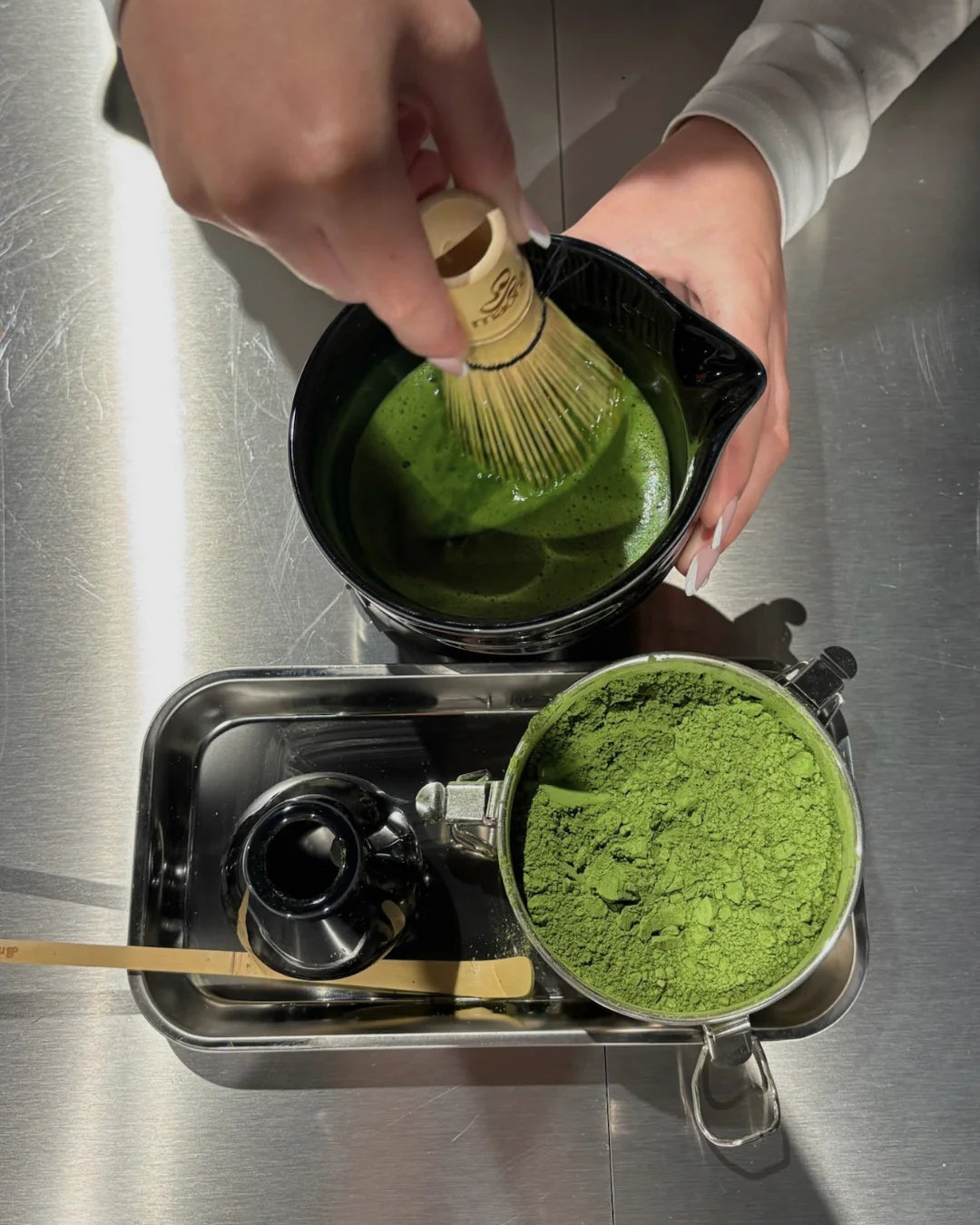 Matcha wird im Chawan mit dem Bambusbesen aufgeschlagen, daneben eine Dose Matcha Pulver