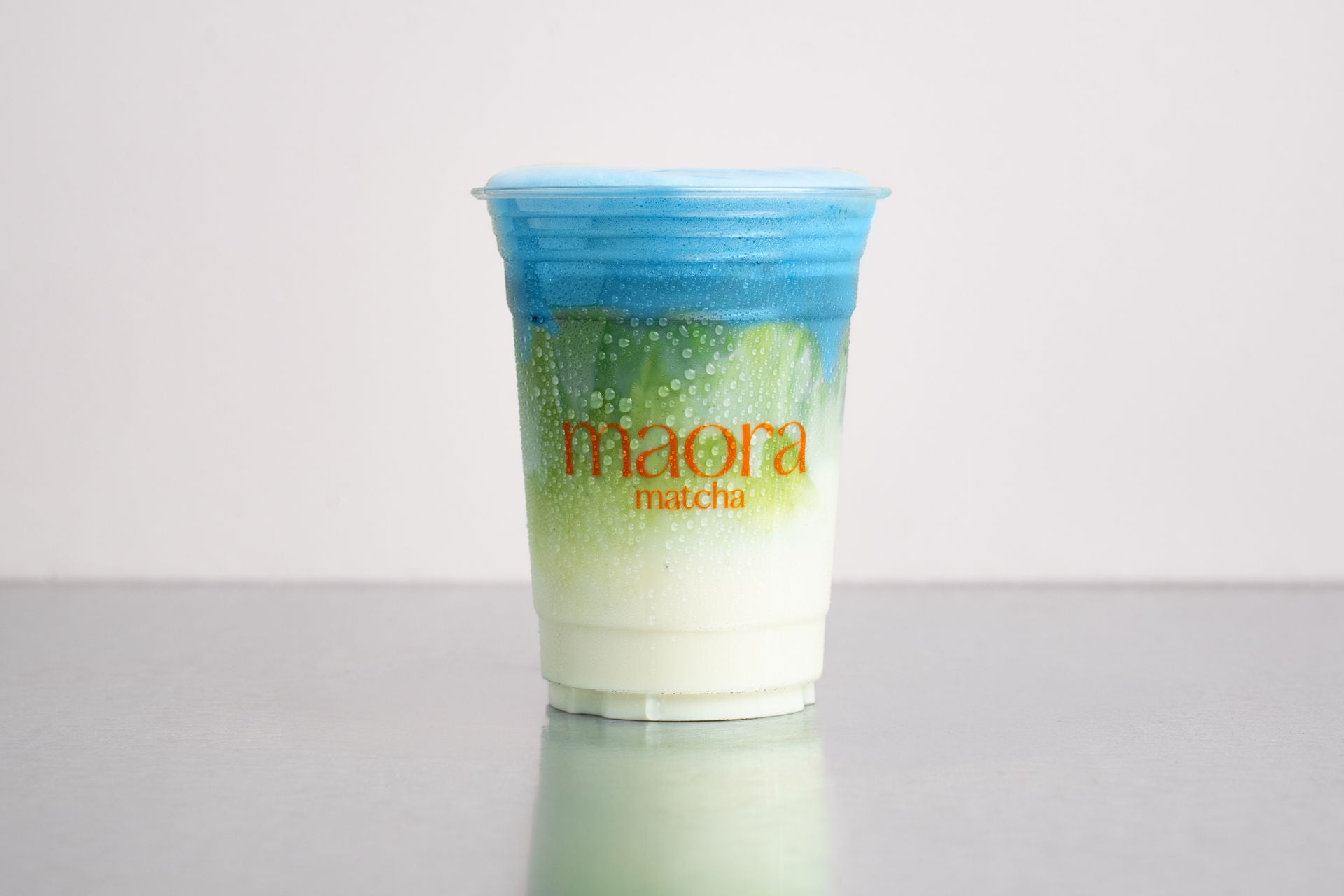 Geschichteter Matcha Drink mit blauer Schicht (Cloud) im Becher mit Maora Logo