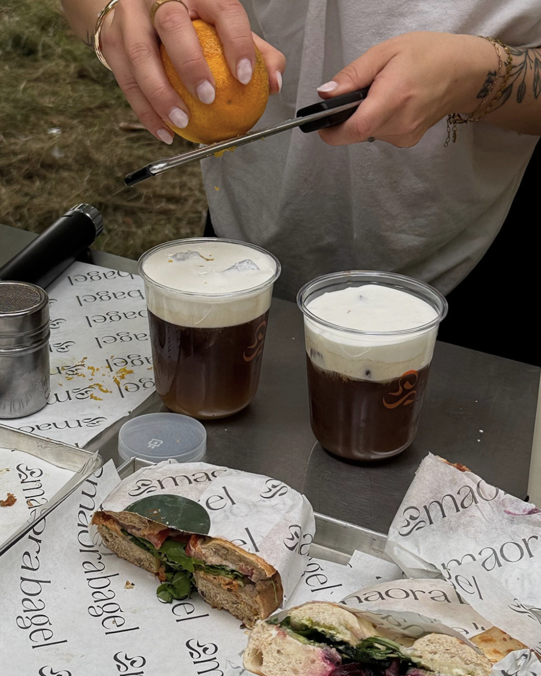 Iced Drinks werden bei einem Sommer Event im Freien mit frischer Orange garniert, daneben Maora Bagels