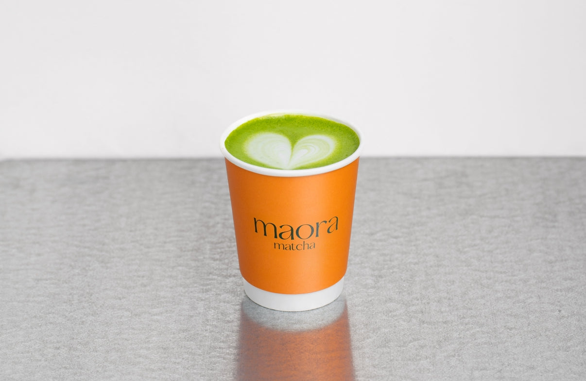 Heißer Matcha Drink im Becher mit Maora Logo

