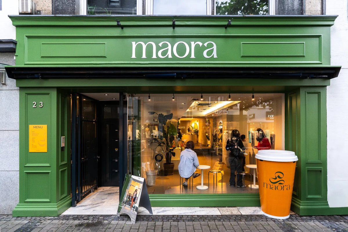 Außenansicht des Maora Matcha Cafés in Köln mit grünem Schaufenster und Einblick in den Innenraum
