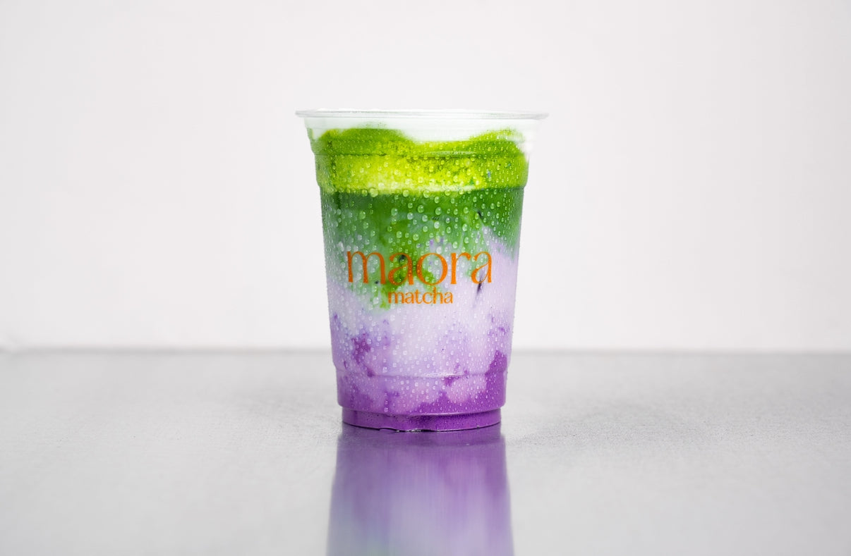 Geschichteter Matcha Drink mit lila Ube Sirup im Becher mit Maora Logo
