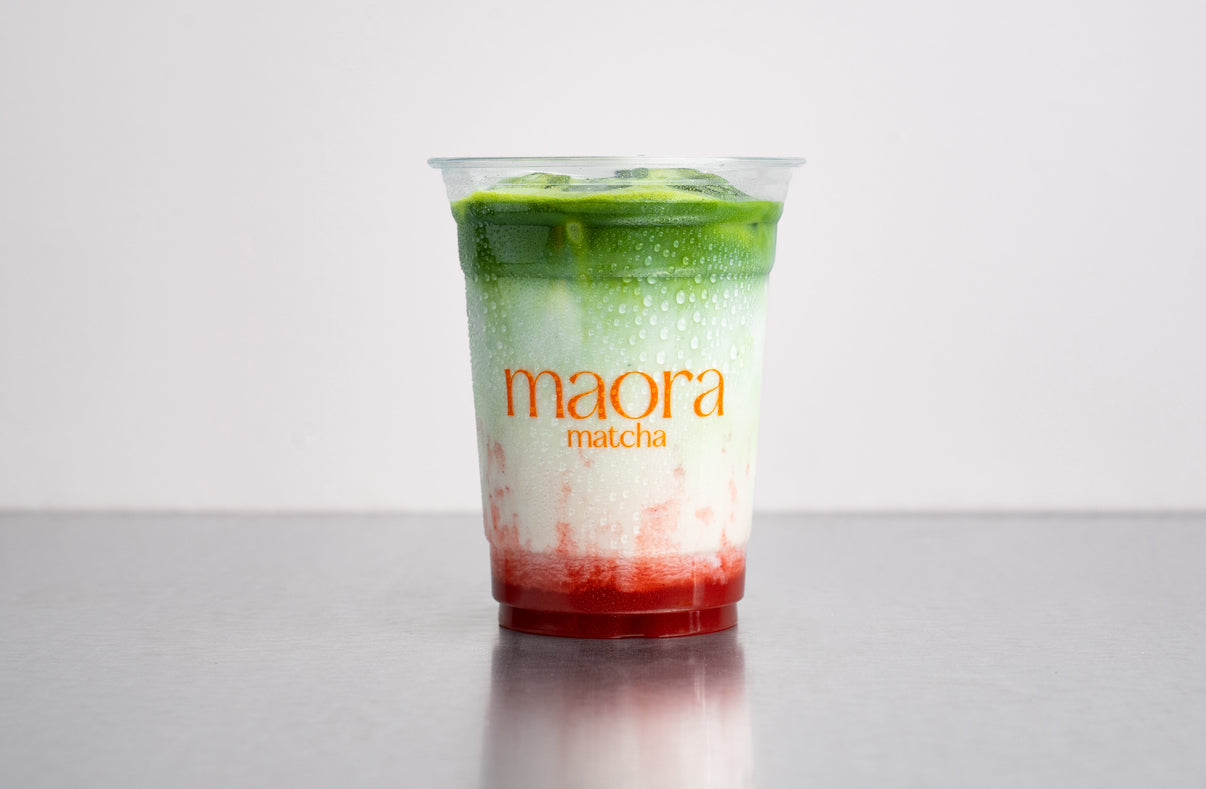 Geschichteter Matcha Drink mit Erdbeer Püree im Becher mit Maora Logo