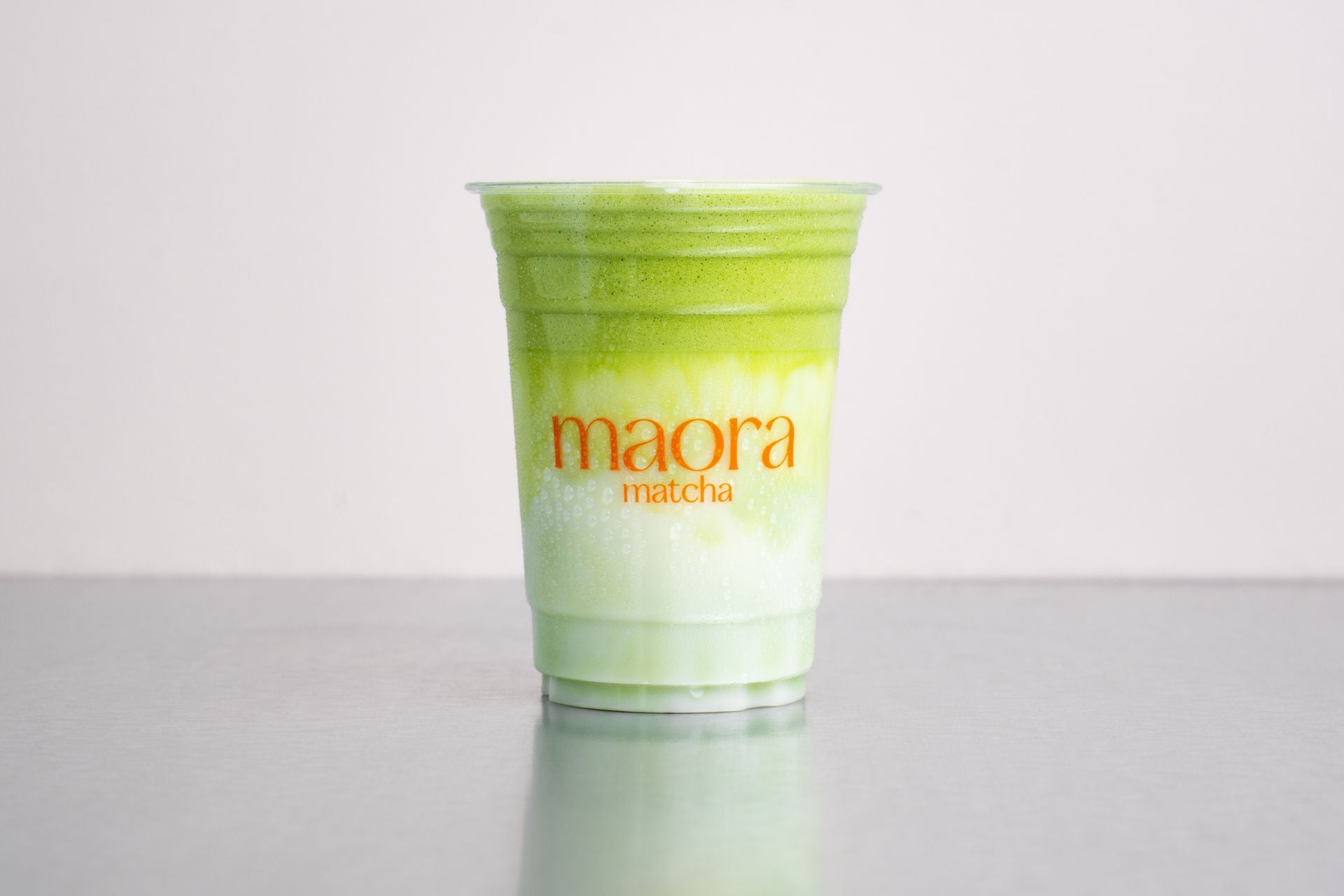 Geschichteter Matcha Drink mit Matcha-Cloud im Becher mit Maora Logo