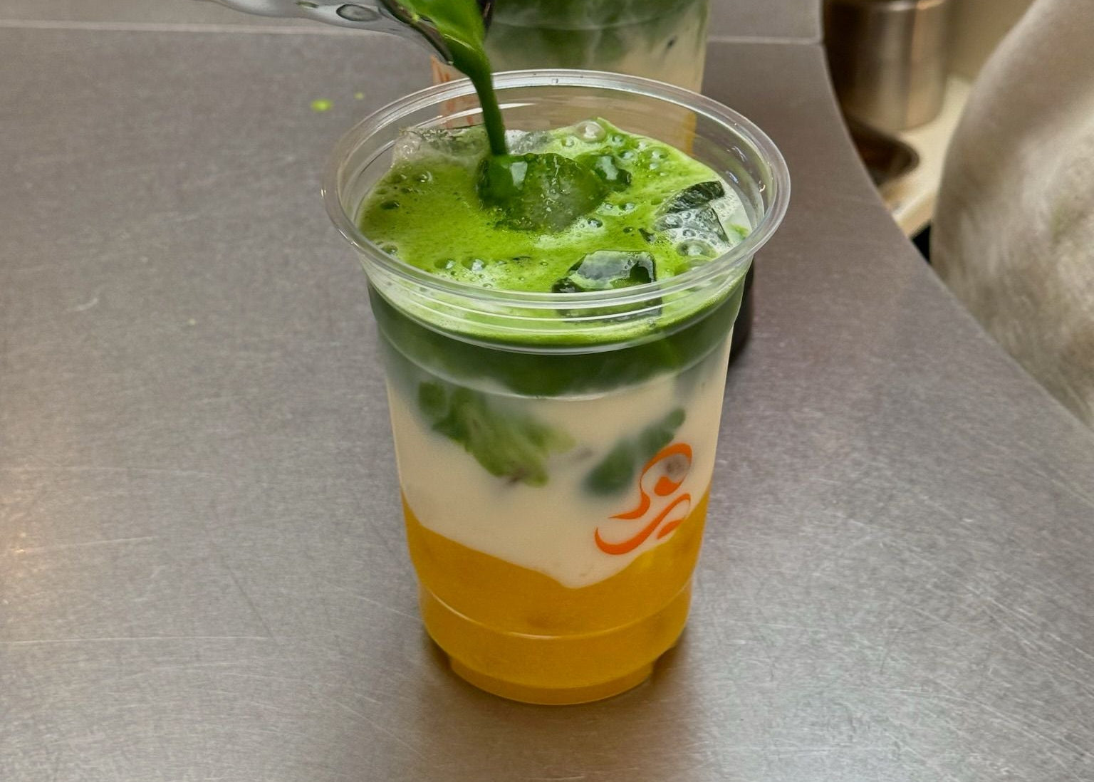 Zubereitung eines Iced Matcha Drinks von Maora im Café, Matcha wird über Eis und Milch gegossen mit Mango Püree
