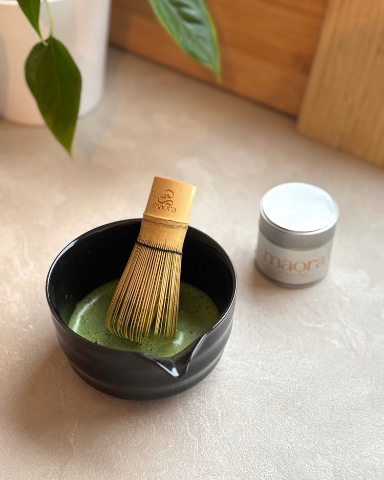 Frisch zubereiteter Matcha in schwarzer Schale mit Bambus Matcha Besen (Chasen), Maora Matcha Dose im Hintergrund