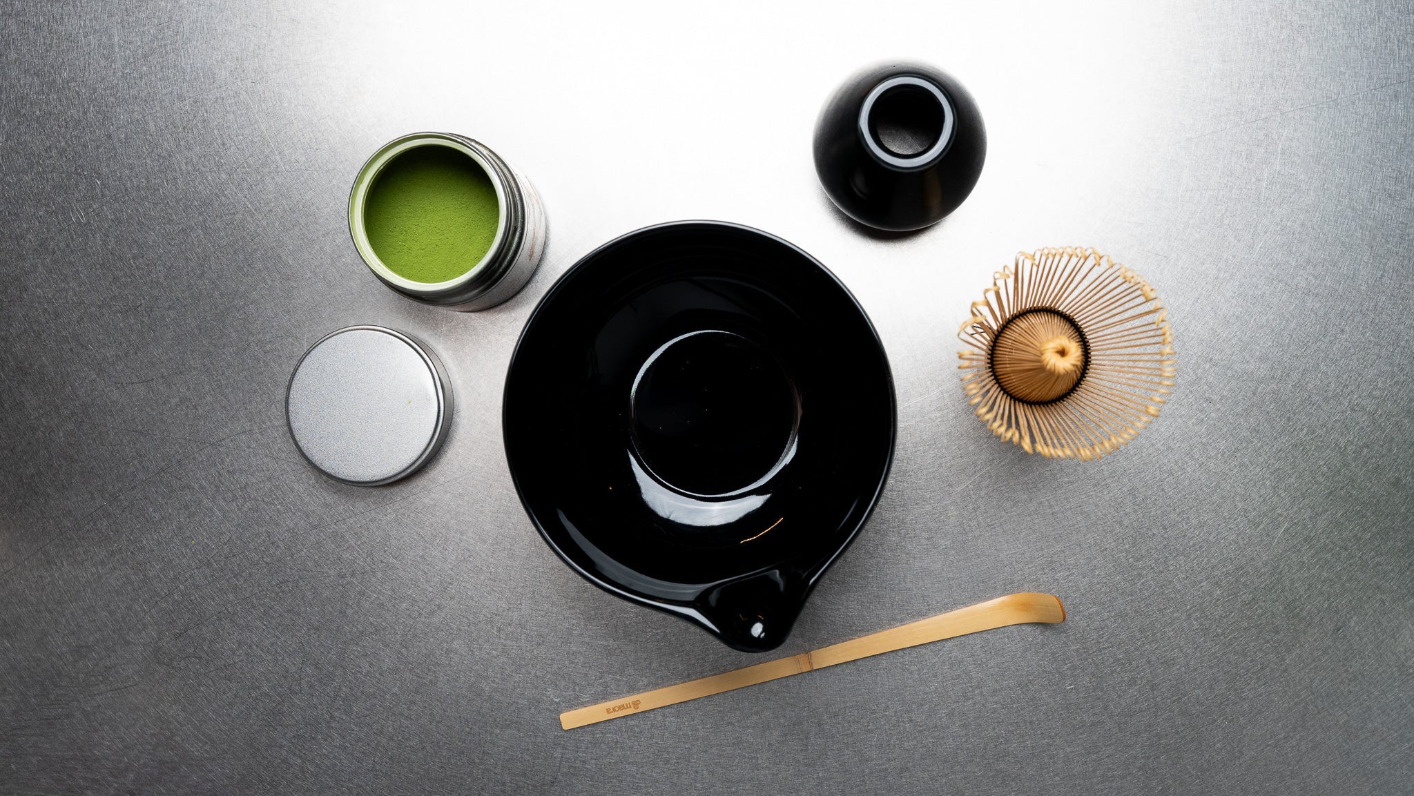Zubehör für die Matcha Zubereitung mit Schale, Bambusbesen, Bambuslöffel und Matcha Pulver von oben fotografiert